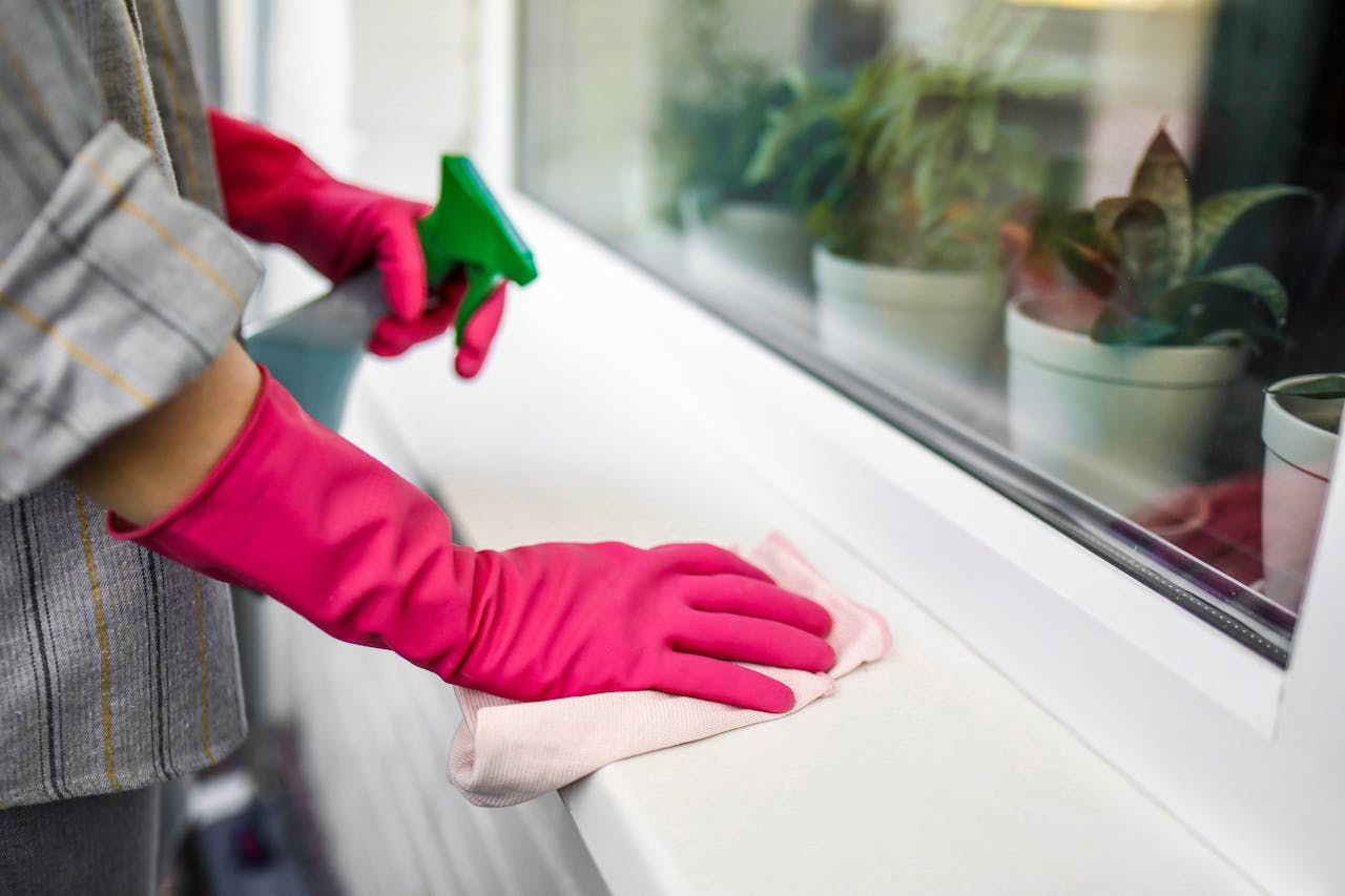 Close-up of hands in pink gloves using spray bottle and cloth indoors.