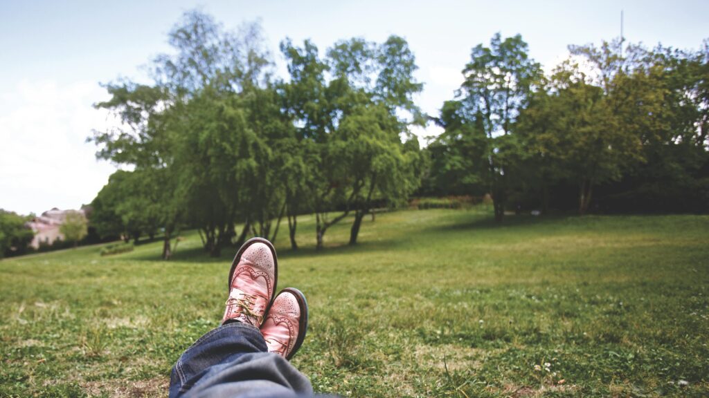A person relaxes in a lush green park, feet up, enjoying a sunny day.