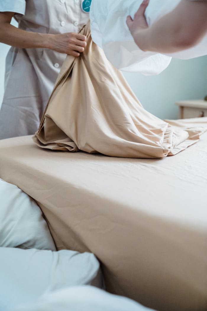 Housekeeper smoothing out bed linens, ensuring neatness in a hotel room setup.
